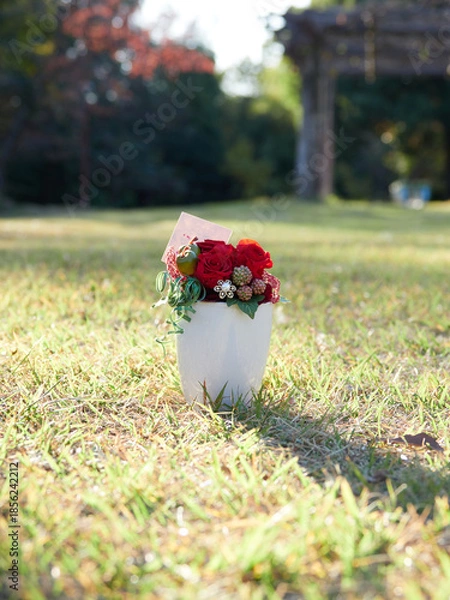 Obraz 秋の昼の公園の芝生にある白い花瓶と鮮やかな造花の様子