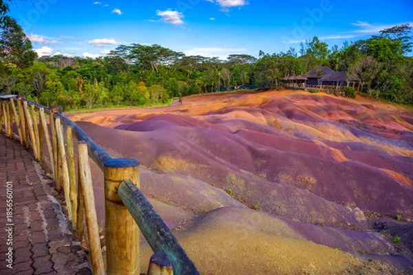 Fototapeta Multicolored sand dunes at Chamarel Seven Colored Earth Geopark with a wooden lodge nestled among trees of a tropical jungle in Mauritius, Africa.