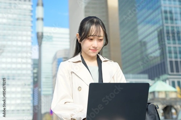 Fototapeta オフィス街でノートパソコンを持つビジネスウーマン