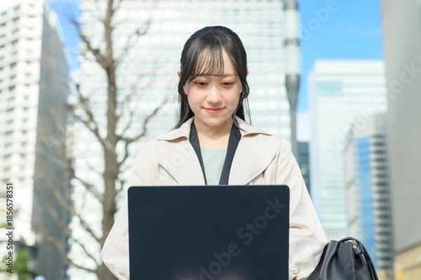Fototapeta オフィス街でノートパソコンを持つビジネスウーマン