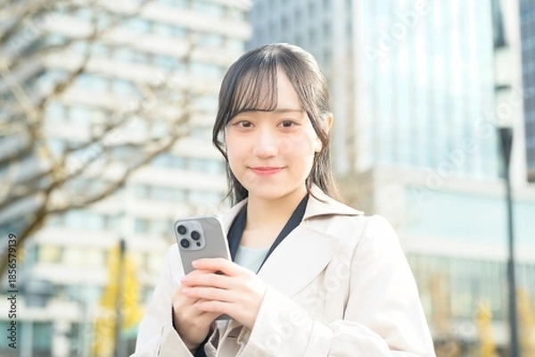 Fototapeta オフィス街でスマホを使用する20代のビジネスウーマン