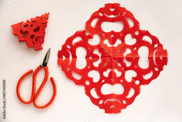 Obraz Red paper cutouts,scissors,and a triangular piece on white background.