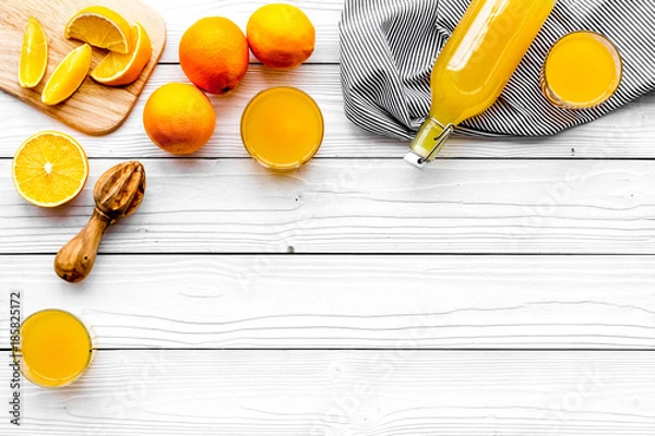 Fototapeta Make orange juice. Juicer, beverage in bottle and glasses near slices of oranges on white wooden background top view copyspace