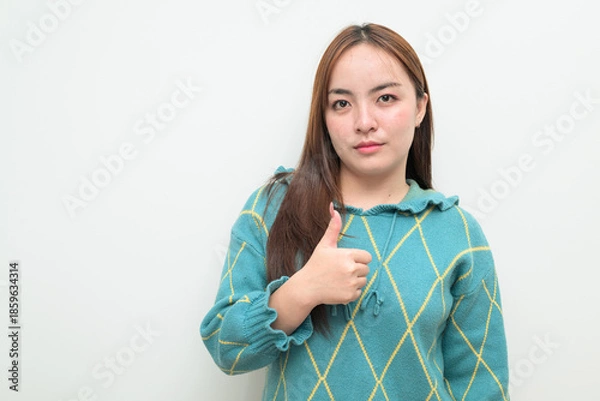 Fototapeta Portrait of a young Asian woman against white background giving thumbs up gesture