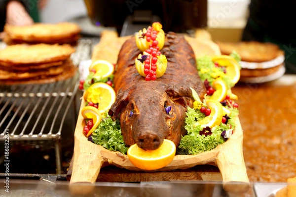 Obraz Grilled suckling piglet in spit roast. Traditional whole pig roasted on barbecue spit. Popular delicious and crispy roasted piggy on christmas fair