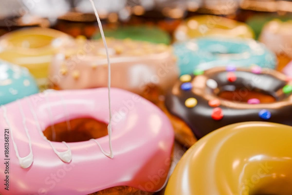 Obraz トレイに並んだカラフルなドーナツに白い液体クリームを垂らす
