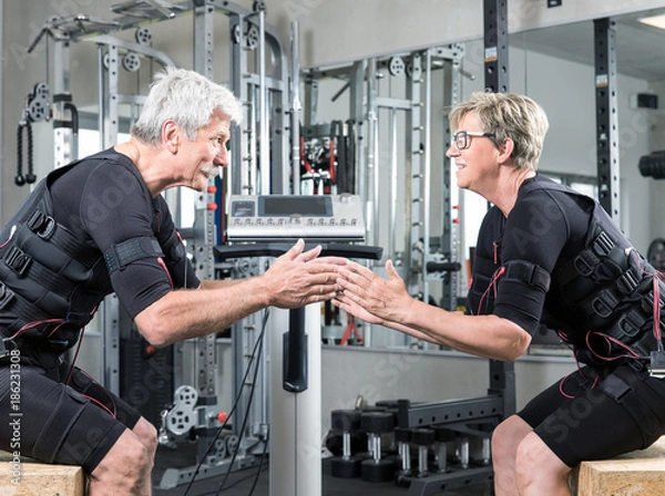Obraz Pärchen im mittleren alter trainiert im Fitnessstudio mit einem EMS Gerät Stromimpulsgerät, Gummibänder, Kurzhanteln