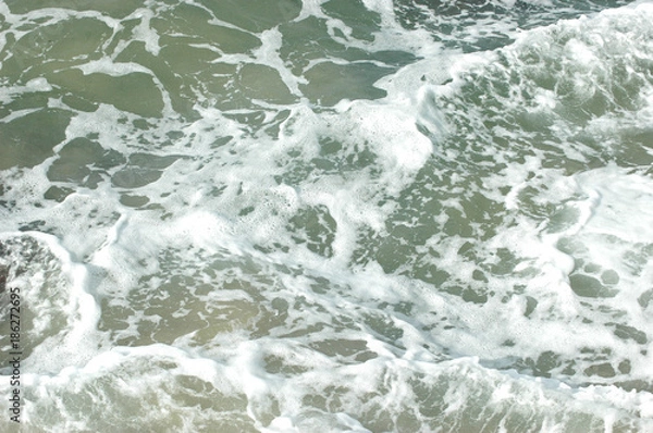 Fototapeta An abstract pattern of white water from waves. The water is shallow, and the sandy ocean floor is visible.