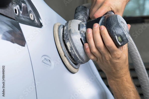 Fototapeta Grinder in the hands of a man who sharpen a car varnish in the car shop.