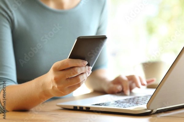 Fototapeta Girl hands using a smart phone and a laptop on a desk