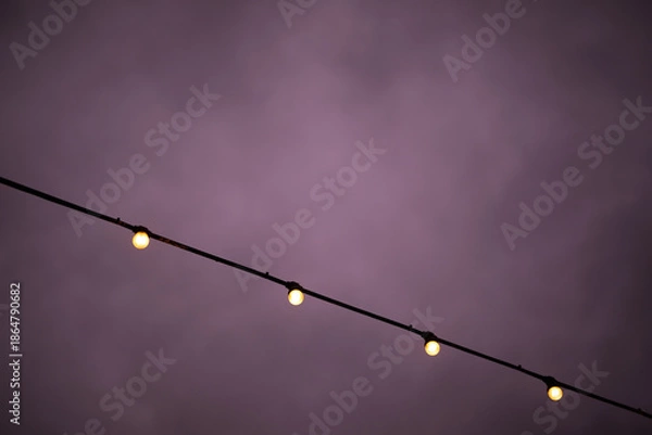 Fototapeta Evening string lights illuminate dark sky