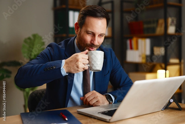 Obraz Businessman drinking coffee while working on laptop in modern office