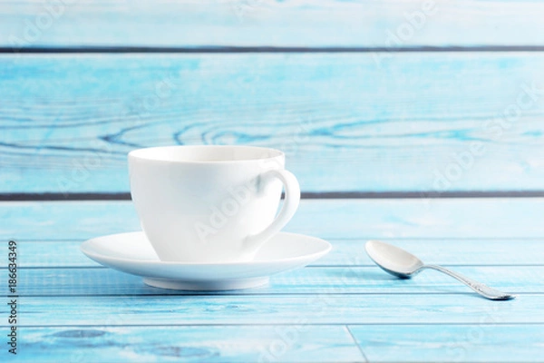 Obraz white mug with saucer and tea spoon on a blue background