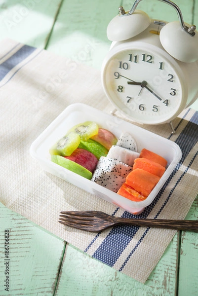 Obraz Mix sliced fruits (papaya,dragon fruit,apple, kiwi) and alarm clock on rustic wooden background