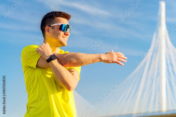Obraz Man stretches before running by a bridge