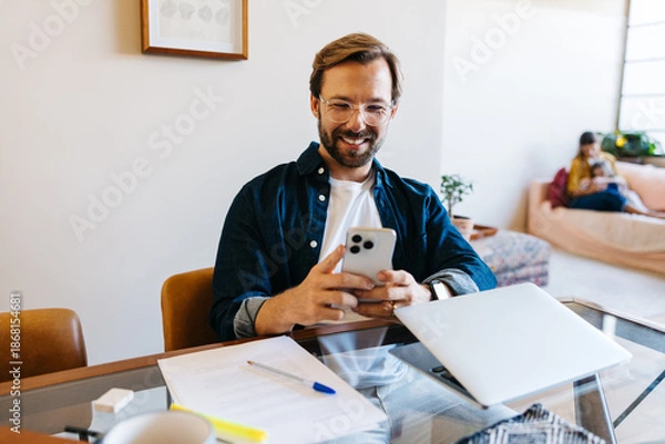 Obraz Businessman smiles while using smartphone at desk