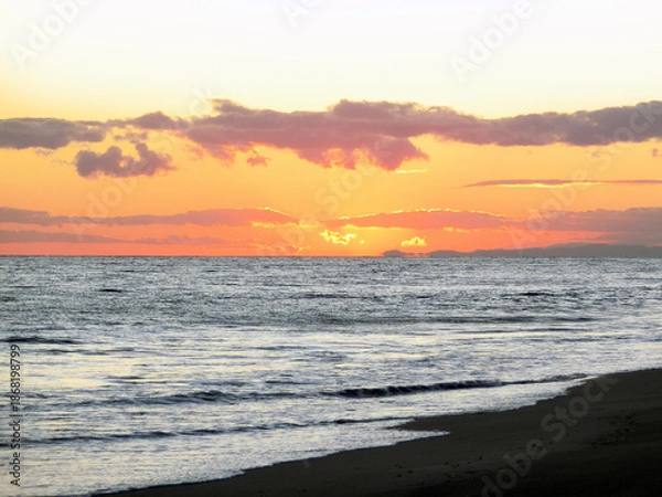 Fototapeta オレンジ色に染まる夕焼けの空模様と穏やかな波打ち際
