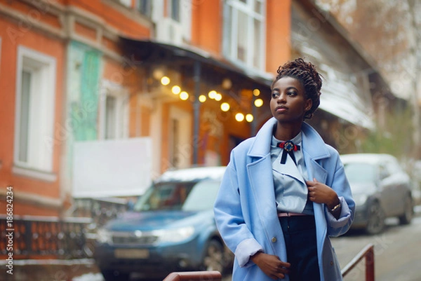 Fototapeta Stylish African girl in the blue coat in the style fashion on the streets with bokeh and cars in the background