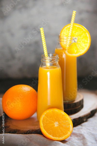 Fototapeta Still life of two bottle full of orange juice and sliced fruits.
