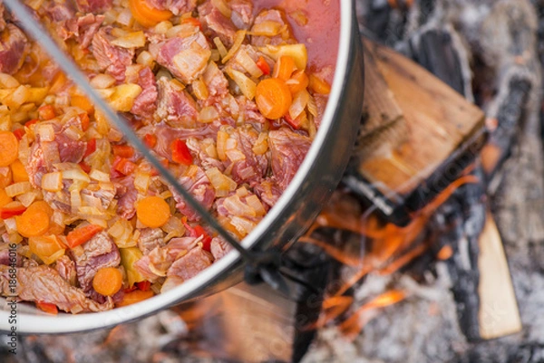 Obraz Boiling, hot goulash soup with meat, paprika, potatoes, onion, carrots is the traditional dish of Hungarian cuisine. Meat stew being prepared in crock pot on open fire. Picnic at the weekend in nature