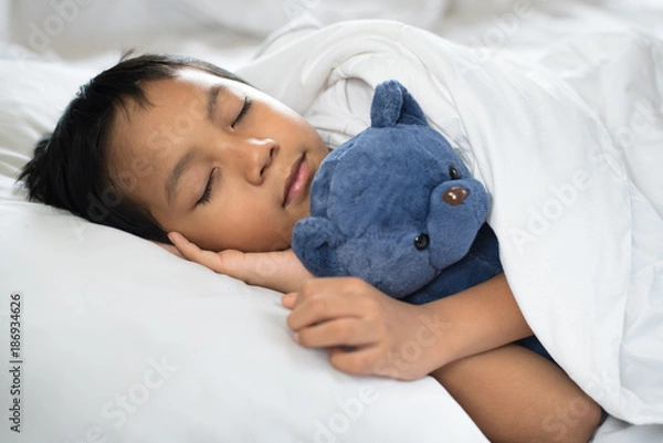 Fototapeta boy sleeping on bed with teddy bear white pillow and sheets.boy fall asleep in morning.sleep concept