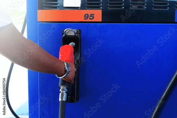 Obraz the red head of fuel supply in slot and the blurred hand of a service man in the service station