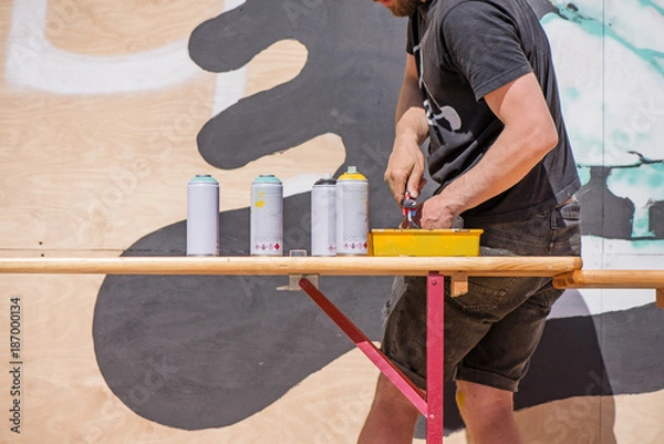 Obraz Male graffiti artist making an abstract drawing on wall with spray colors in sunny summer day 