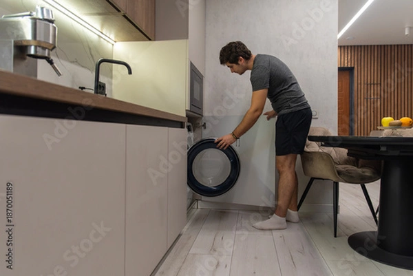 Obraz Man loading laundry into front-load washing machine at home