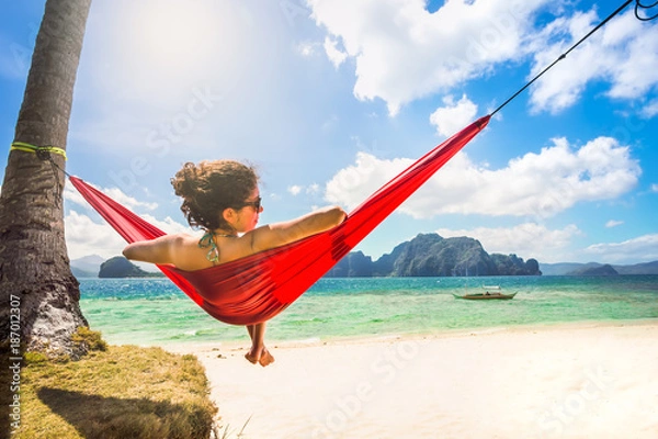 Obraz Young caucasian female relaxing in a red hammock on a tropical b