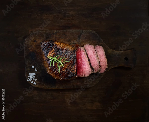 Fototapeta grilled steak with rosemary on a cutting board on a black background