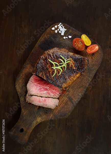 Fototapeta grilled steak with rosemary on a cutting board on a black background