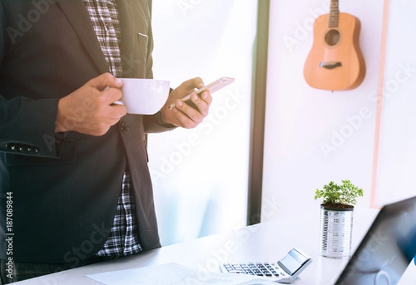 Fototapeta Businessmen are standing relaxed, holding a cup of coffee while they are using the smart phone.Business people are using the phone to contact a partner.Online shopping concept. mobile banking concept.