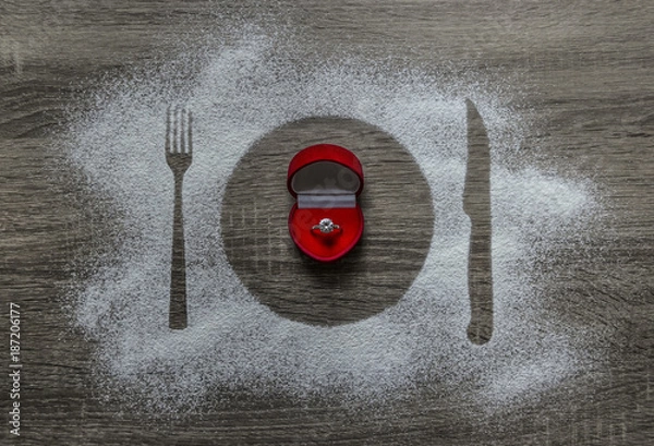 Fototapeta on a wooden background with powdered powder snow covered with a silhouette a plate a fork knife of appliances in the center lies a box with a ring with a diamond 