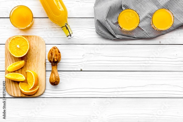 Fototapeta Make orange juice. Juicer, beverage in bottle and glasses near slices of oranges on white wooden background top view copyspace