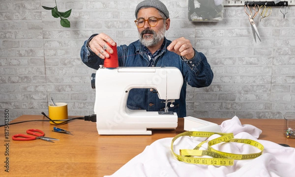 Obraz Man threading a sewing machine for tailoring project