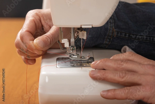 Obraz Hands threading red yarn into sewing machine needle