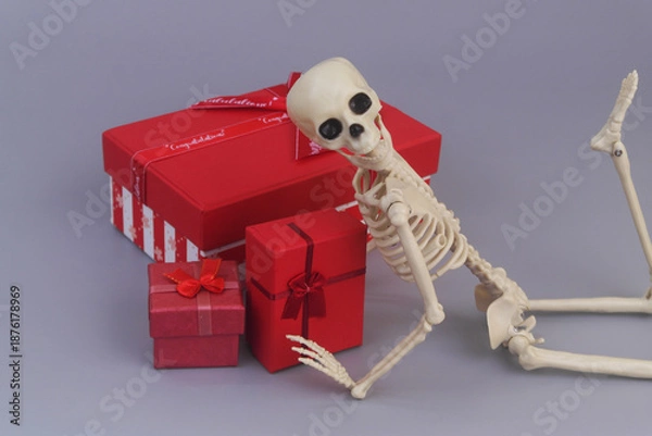 Obraz Human skeleton with red gift boxes on grey background.