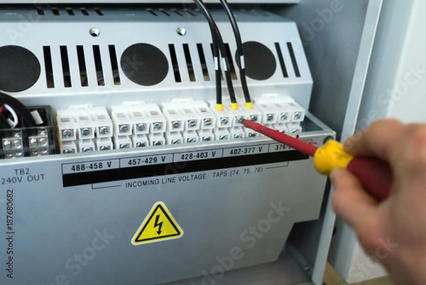 Obraz Hand of electrician with screwdriver tighten up electric terminals of transformer in electric cabinet of cnc machine