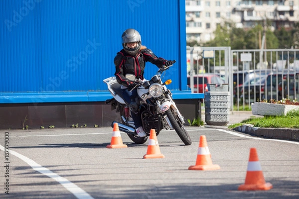 Fototapeta Kierowca L przejeżdżający slalomem przez pomarańczowe pachołki na motordromie na motocyklu