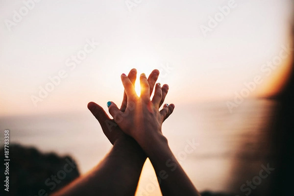 Fototapeta man and woman holding each other's hands against the sky and the sea on the sunset