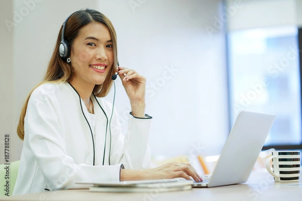 Fototapeta close up focus on asian call centre woman with headphone trying to response answer or working in operation office room.helpdesk hotline concept.
