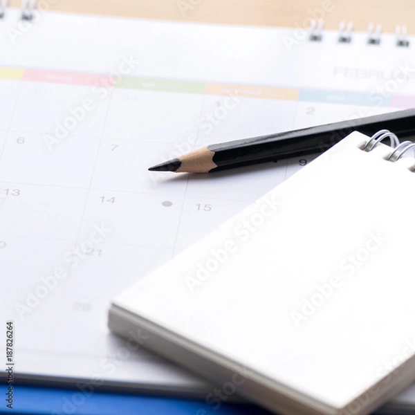 Fototapeta Notepad with pencil, calendar  on wood board blurry background.using wallpaper for education, business photo.Take note of the product for book with paper and concept, object or copy space.