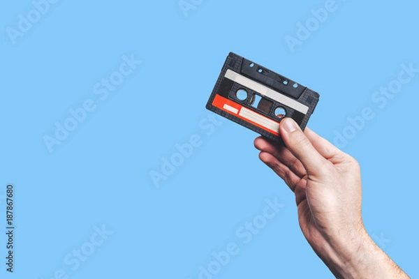 Fototapeta Hand holding  cassette tape. Used cassette tape. Audio cassette. Vintage audio cassette tap in the hand. Old cassette tape audio isolated on color background.