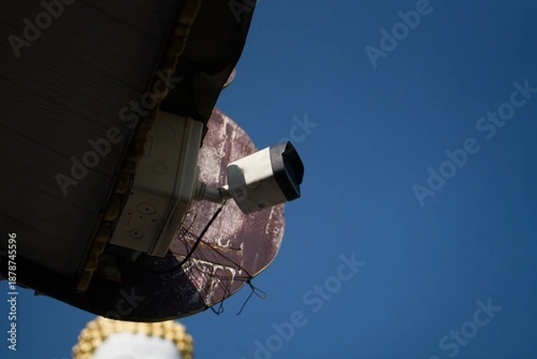 Obraz Security Camera Mounted on a Building Under a Clear Blue Sky