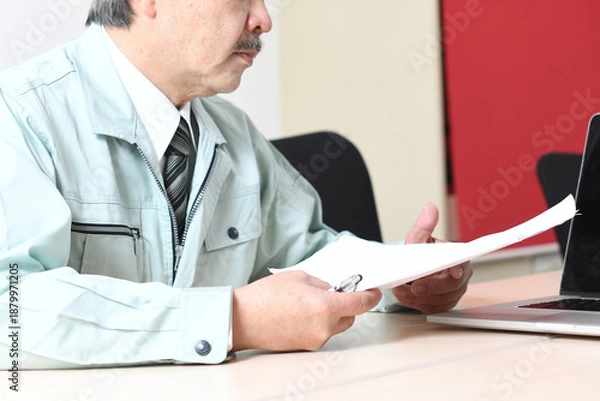 Obraz 商談中に書類を確認する作業服姿の中年男性