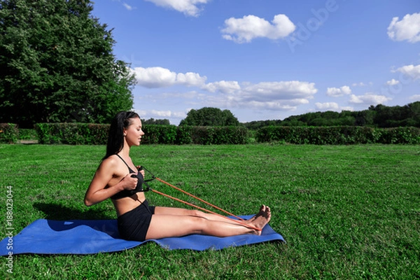 Obraz Female athlete doing exercises with expander in the Park on the grass.