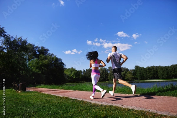 Fototapeta Woman and man running in the Park along the path near the lake.