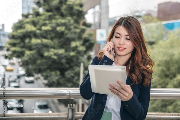 Obraz Portraits of beautiful asian woman look confidence is standing and holding cellphone . she using smartphone calling to conversation with customer.
