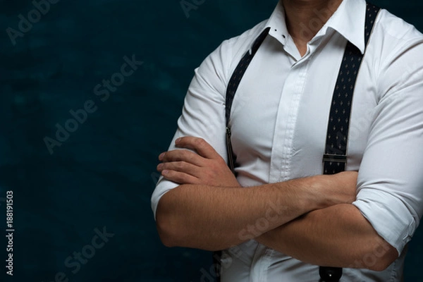 Fototapeta Hands of an unidentified strong man in formal attire with suspenders folded on chest on blue grunge background
