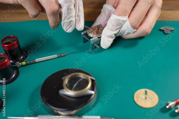 Obraz Professional watchmaker works on assembling a mechanical watch movement using precision tools on a clean workbench in a workshop.